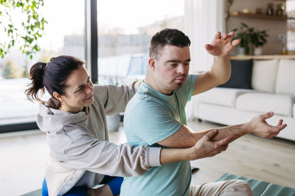 Young man with Down syndrome exercising at home with his mother. Workout routine for disabled man.