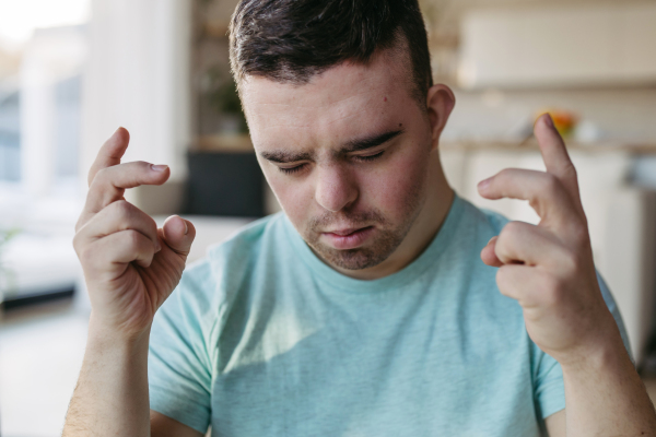 Young man with Down syndrome is focused, eyes closed. Disabled man making a wish, wanting, hoping for something.