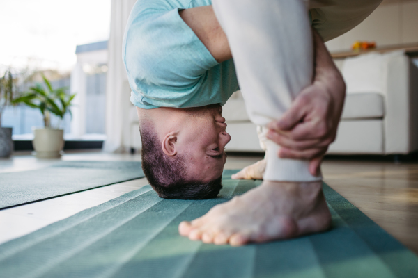 Young man with Down syndrome exercising at home, stretching his body, legs. Workout routine for disabled man.