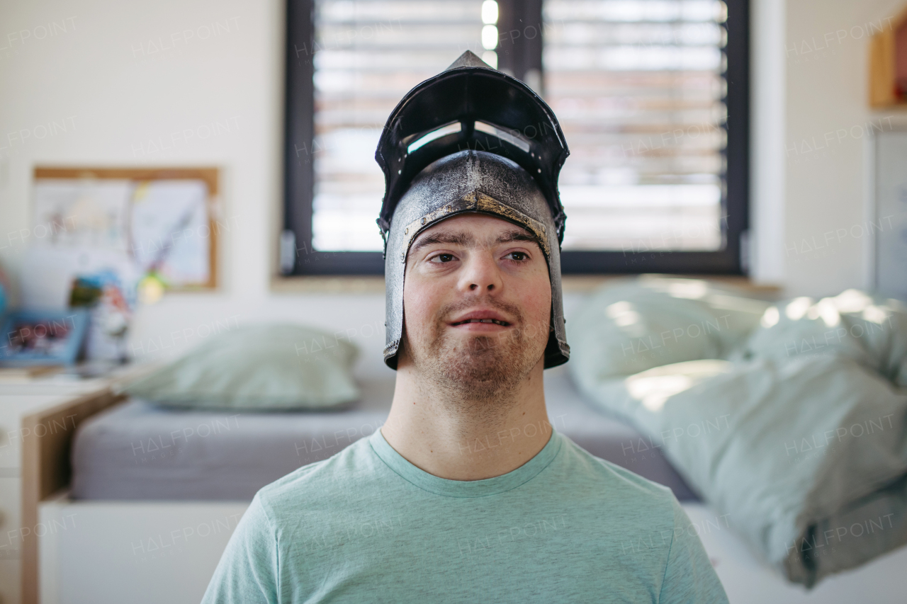 Portrait of happy smiling man with down syndrome at home, with knight's helmet on head.