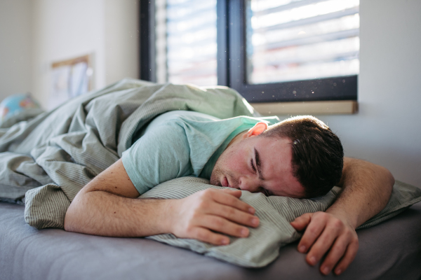 Young man with down syndrome sleeping in his bed. Lying on his abdomen, resting in bedroom.