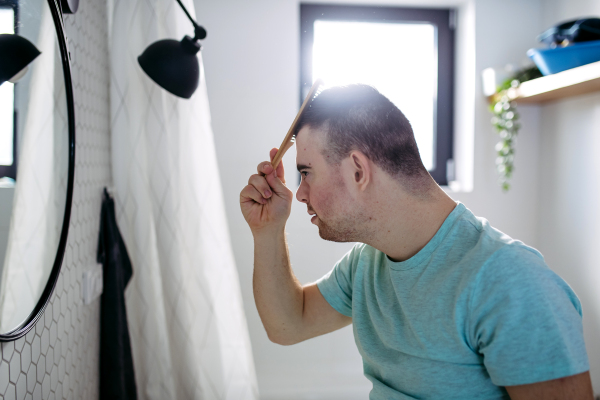 Side view of young man with down syndrome in bathroom, combing his hairs.