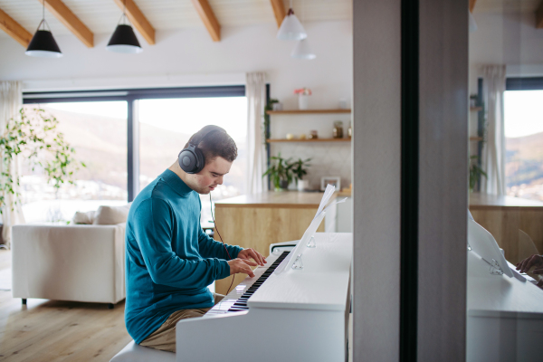 Young man with down syndrome playing on piano, listening his music via headphones. Practicing piano with headphones