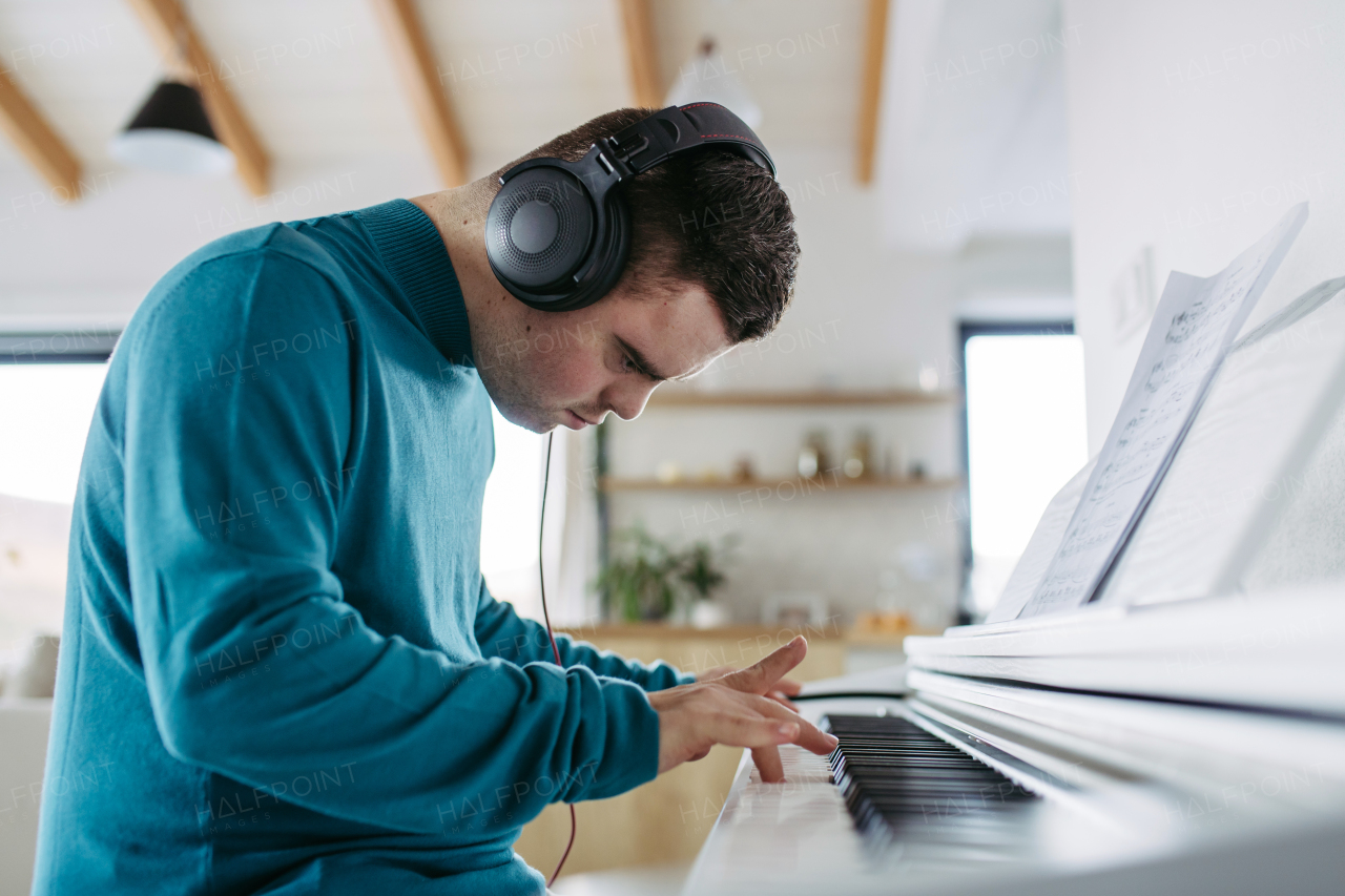 Young man with down syndrome playing on piano, listening his music via headphones. Practicing piano with headphones