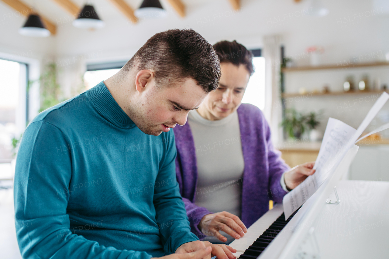 Young man with down syndrome and his mother playing on piano, making music at home. Practicing piano with music teacher.