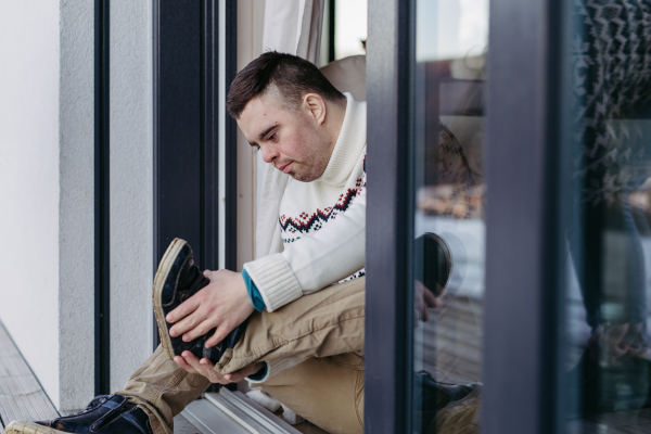 Portrait of young man with Down syndrome putting on shoes, sitting on the floor.