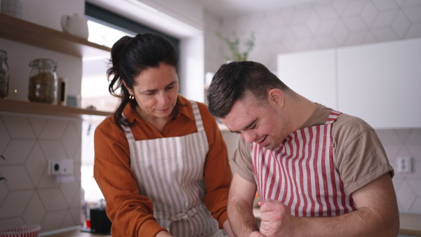 A close up of young man with Down syndrome preparig dough for cookies with his mom at home. Everyday routine for man with Down syndrome.