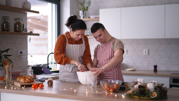 Young man with Down syndrome preparing breakfast with his mother at home, cracking eggs. Morning routine for man with Down syndrome genetic disorder.