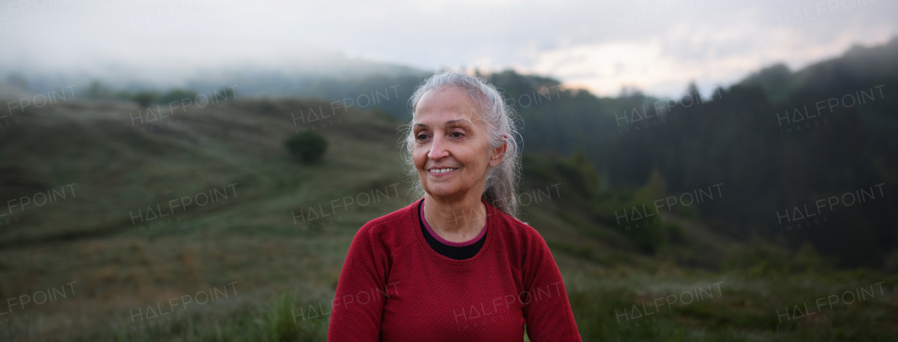 A senior woman hiking in nature on early morning with fog and mountains in background.