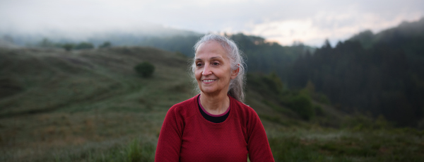 A senior woman hiking in nature on early morning with fog and mountains in background.