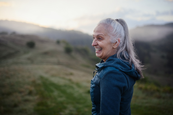 A senior woman hiking in nature on early morning with fog and mountains in background.