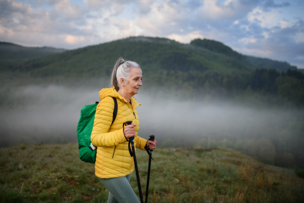 A senior woman hiking in nature on early morning with fog and mountains in background.