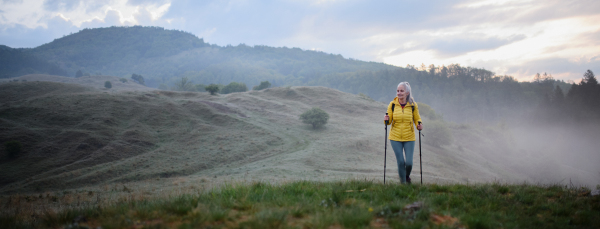 A senior woman jogging in nature on early morning with fog and mountains in background.