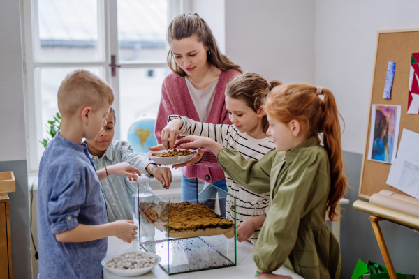 Young teacher making a little greenhouse with their pupils, learning them about planting.