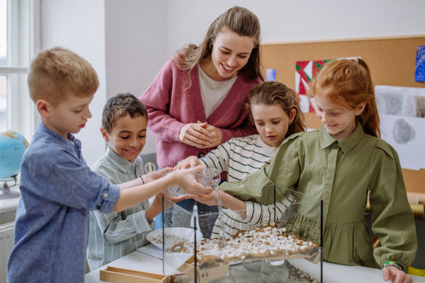 Young teacher making a little greenhouse with their pupils, learning them about planting.