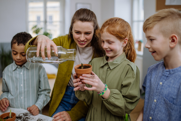 Young teacher learning her pupils how to take care about plants.