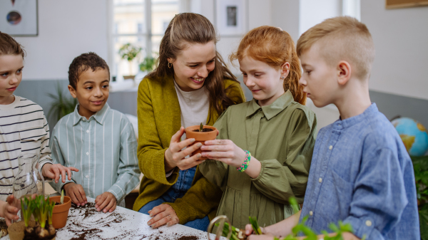 Young teacher learning her pupils how to take care about plants.