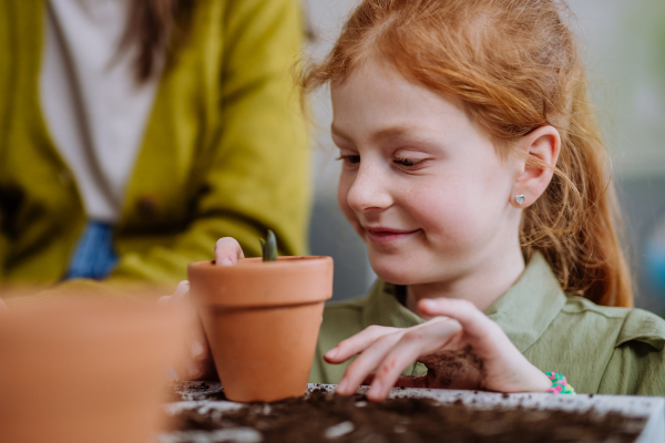 Happy little girl looking at growing plant in a ceramics pot.