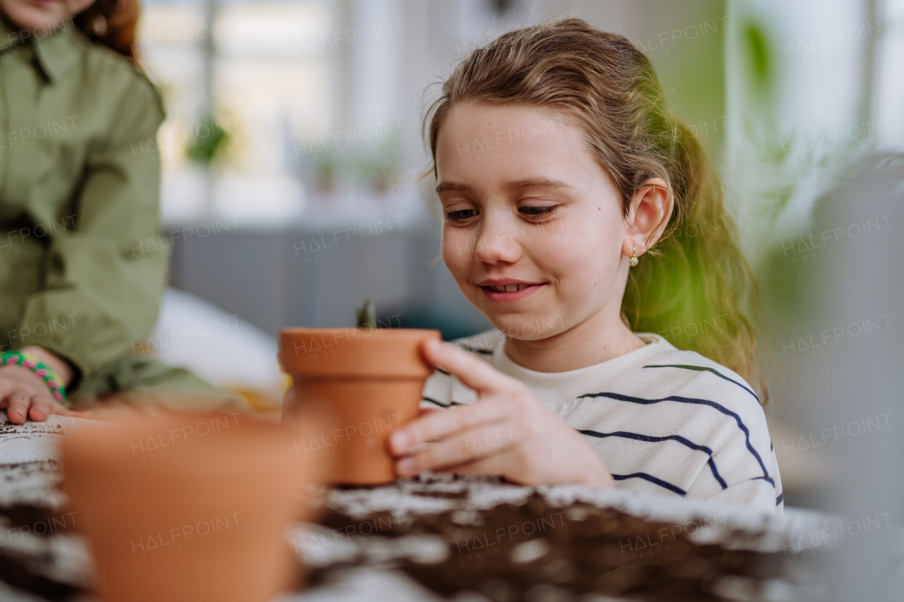 Happy little girl looking at growing plant in a ceramics pot.