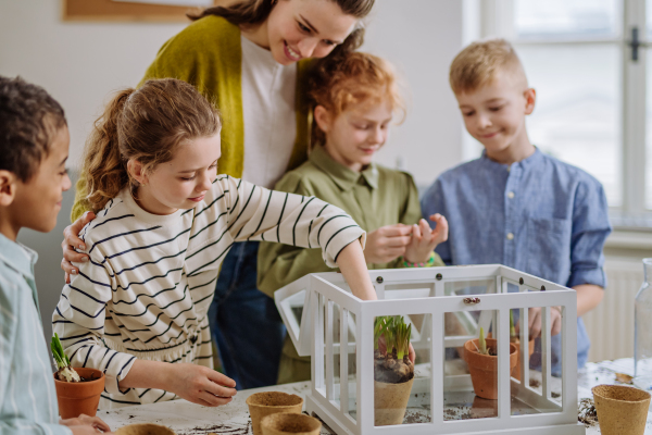 Young teacher learning her pupils how to take care about plants.