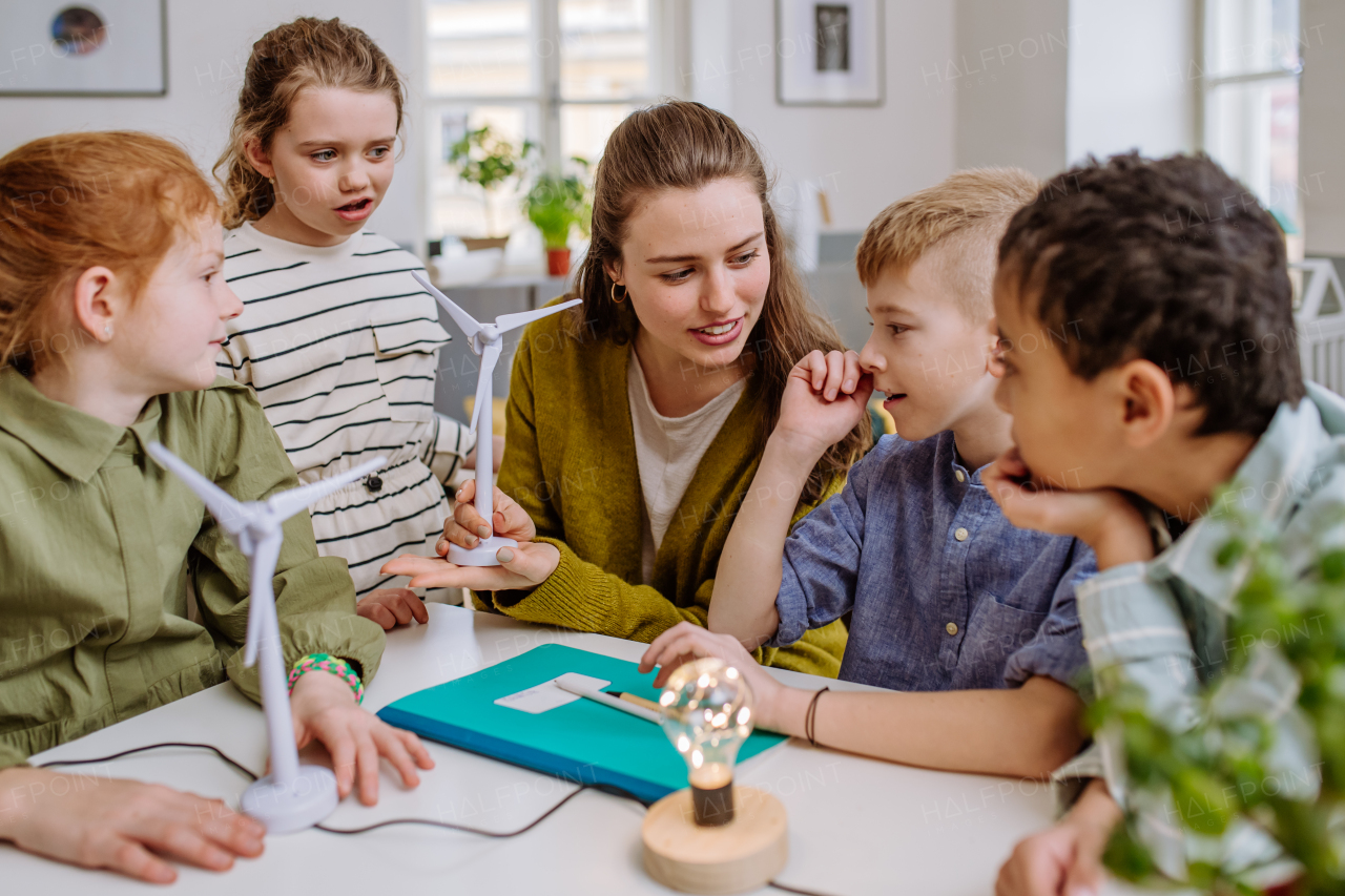 Young teacher with model of wind turbine learning her pupils about wind energy.