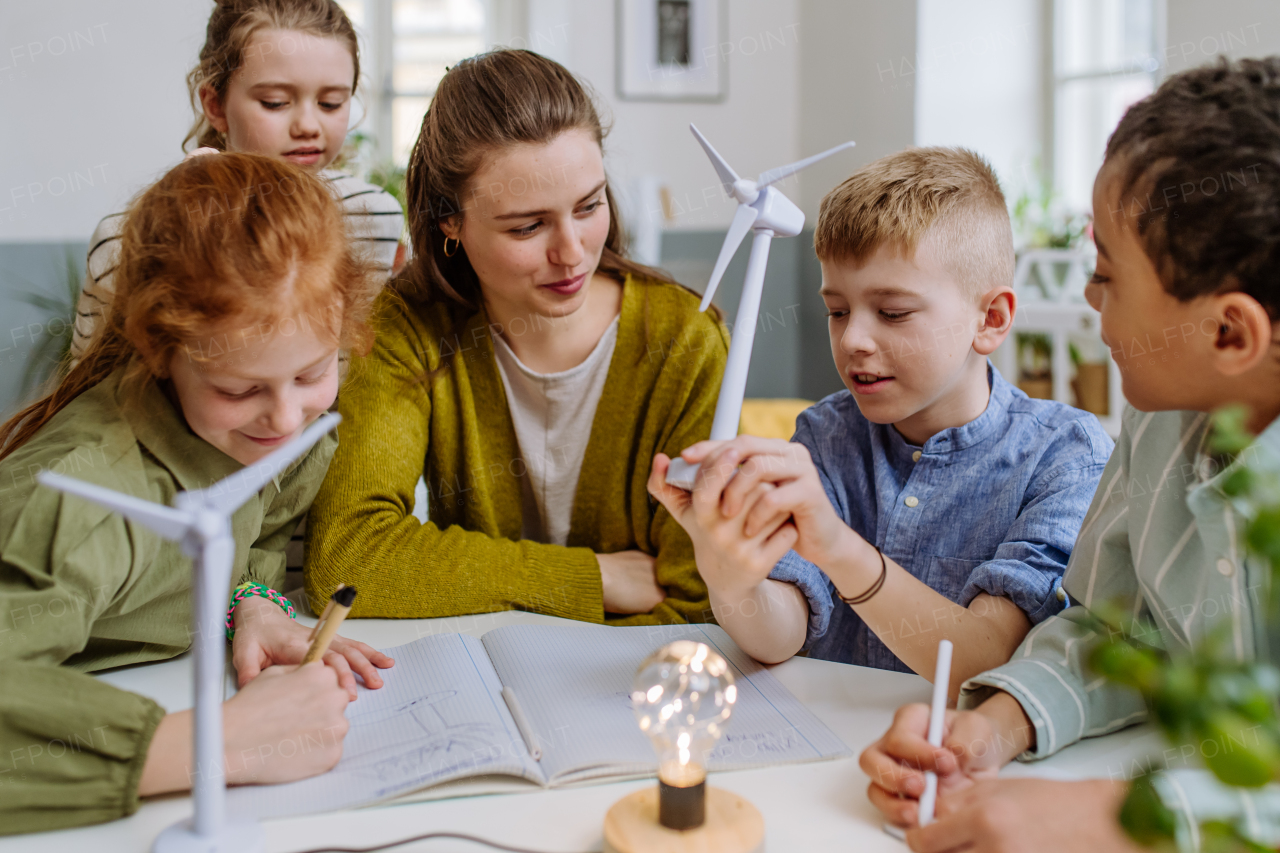 Young teacher with model of wind turbine learning her pupils about wind energy.