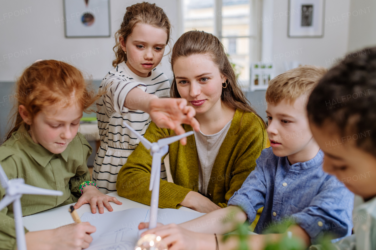 Young teacher with model of wind turbine learning her pupils about wind energy.