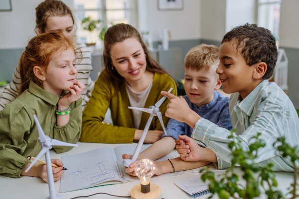 Young teacher with model of wind turbine learning her pupils about wind energy.