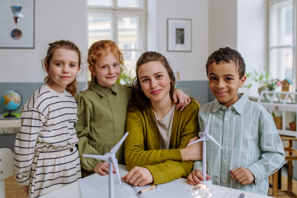 Young teacher with model of wind turbine learning her pupils about wind energy.