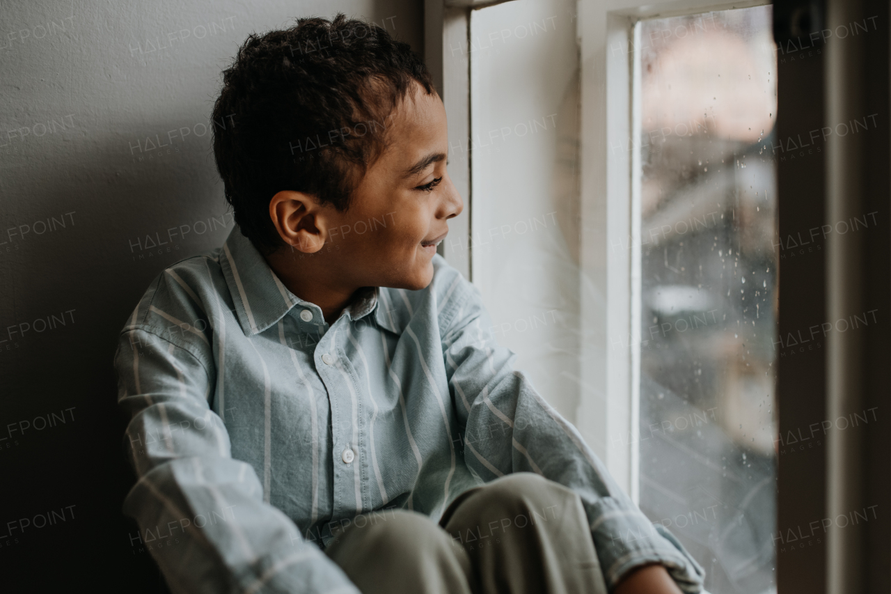 Little multiracial boy looking out of the window.