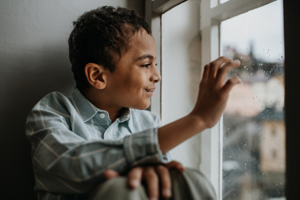 Little multiracial boy looking out of the window.