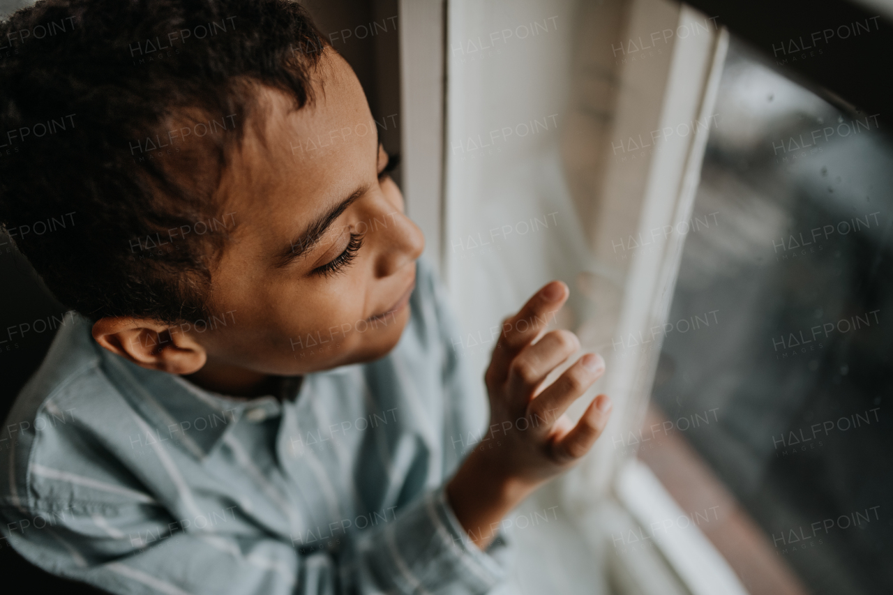 Little multiracial boy looking out of the window.