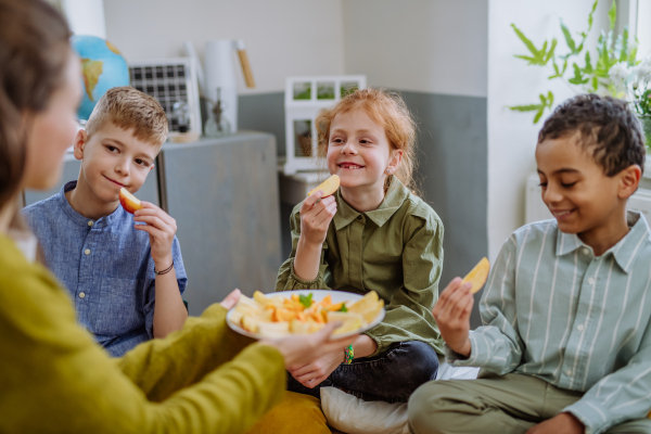 Teacher giving healthy fruit snack for pupils in school.