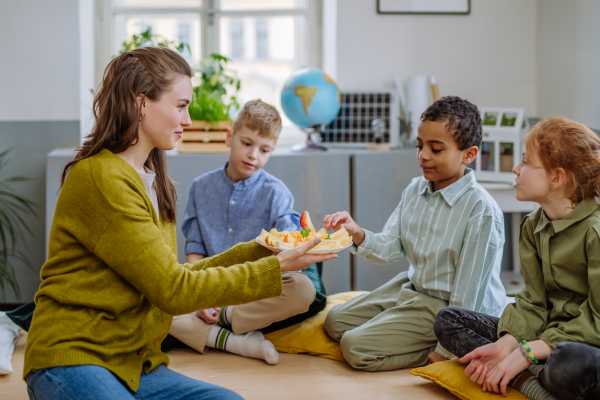 Teacher giving healthy fruit snack for pupils in school.