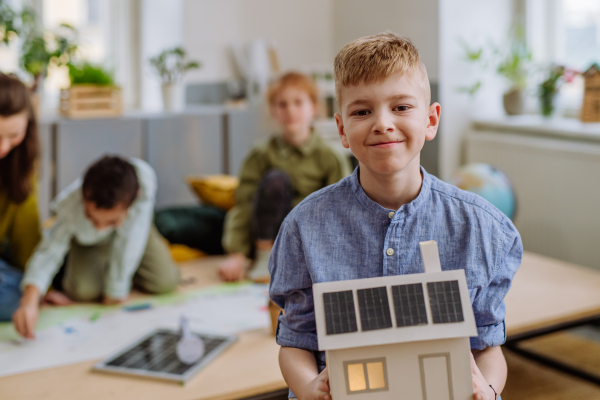 Little boy posing with a model of house with solar system during school lesson.