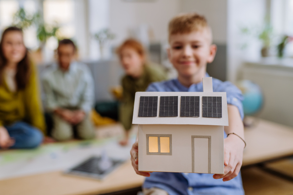 Little boy posing with a model of house with solar system during school lesson.