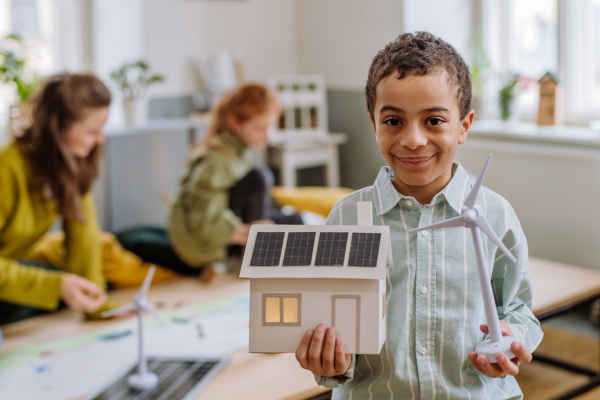 Little boy posing with a model of wind turbine and model of house with solar system during school lesson.