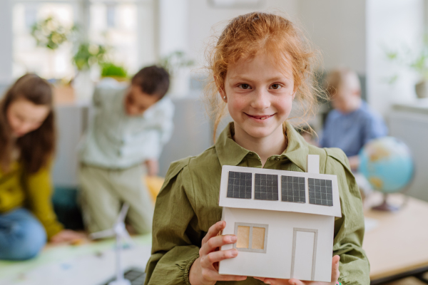 Little girl posing with a model of house with solar system during school lesson.