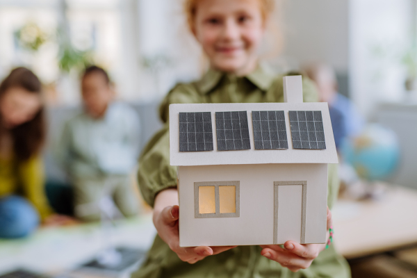 Little girl posing with a model of house with solar system during school lesson.