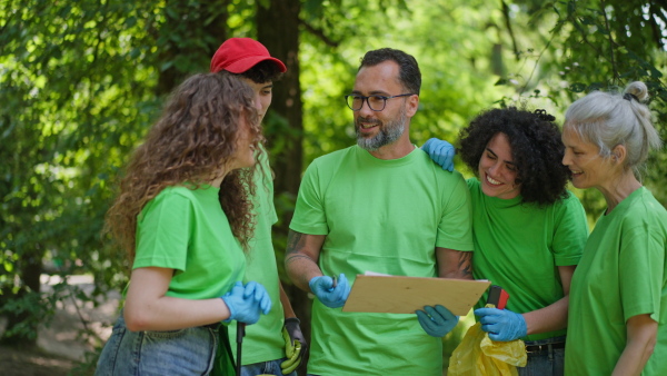 Group of volunteers picking trash, removing litter from forest, protecting nature and wildlife. Forest cleanup. Environmental education program by local community.