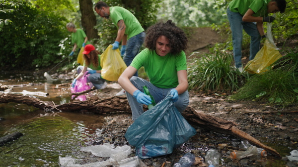 Group of volunteers picking trash, removing litter stream in forest, protecting nature and wildlife. Forest cleanup. Environmental education program by local community.