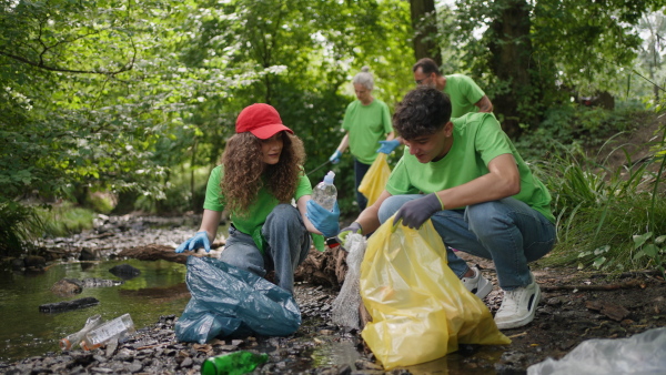 Group of volunteers picking trash, removing litter stream in forest, protecting nature and wildlife. Forest cleanup. Environmental education program by local community.