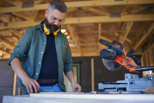 Construction worker working with the eletric saw inside wooden construction of house, diy eco-friendly homes concept.