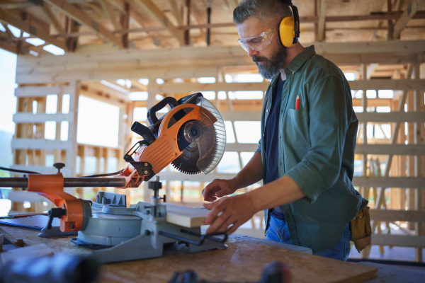 Construction worker working with eletric saw inside a wooden construction of house, diy eco-friendly homes concept.