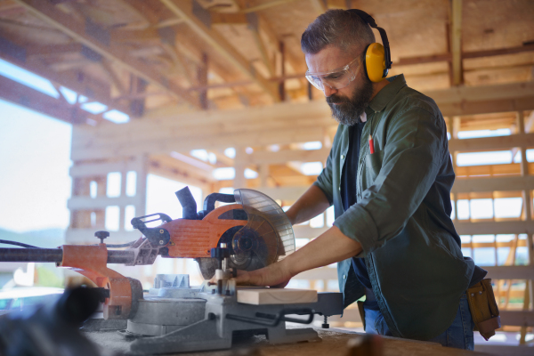 Construction worker working with eletric saw inside a wooden construction of house, diy eco-friendly homes concept.