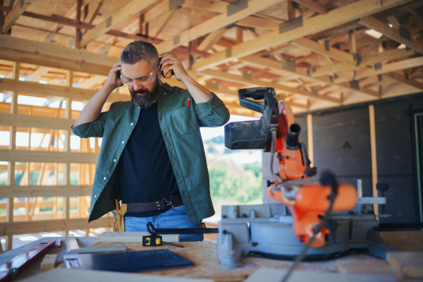 Construction worker working with the eletric saw inside wooden construction of house, diy eco-friendly homes concept.