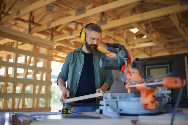 Construction worker working with the eletric saw inside wooden construction of house, diy eco-friendly homes concept.