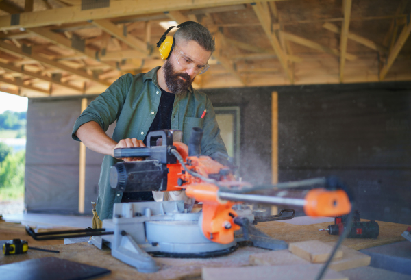 Construction worker working with eletric saw inside a wooden construction of house, diy eco-friendly homes concept.