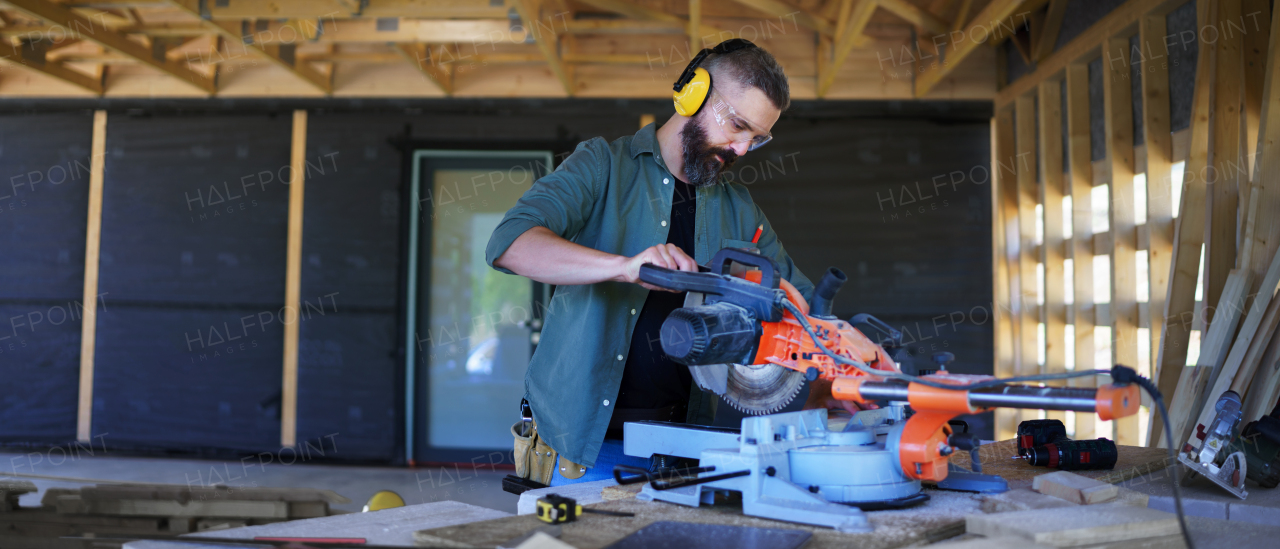 Construction worker working with eletric saw inside a wooden construction of house, diy eco-friendly homes concept.