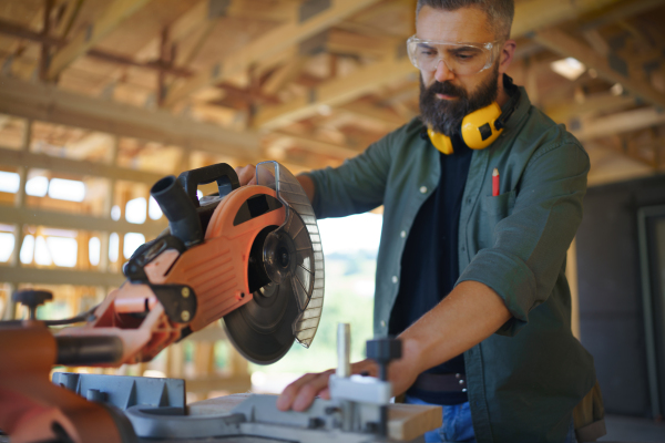 Construction worker working with the eletric saw inside wooden construction of house, diy eco-friendly homes concept.